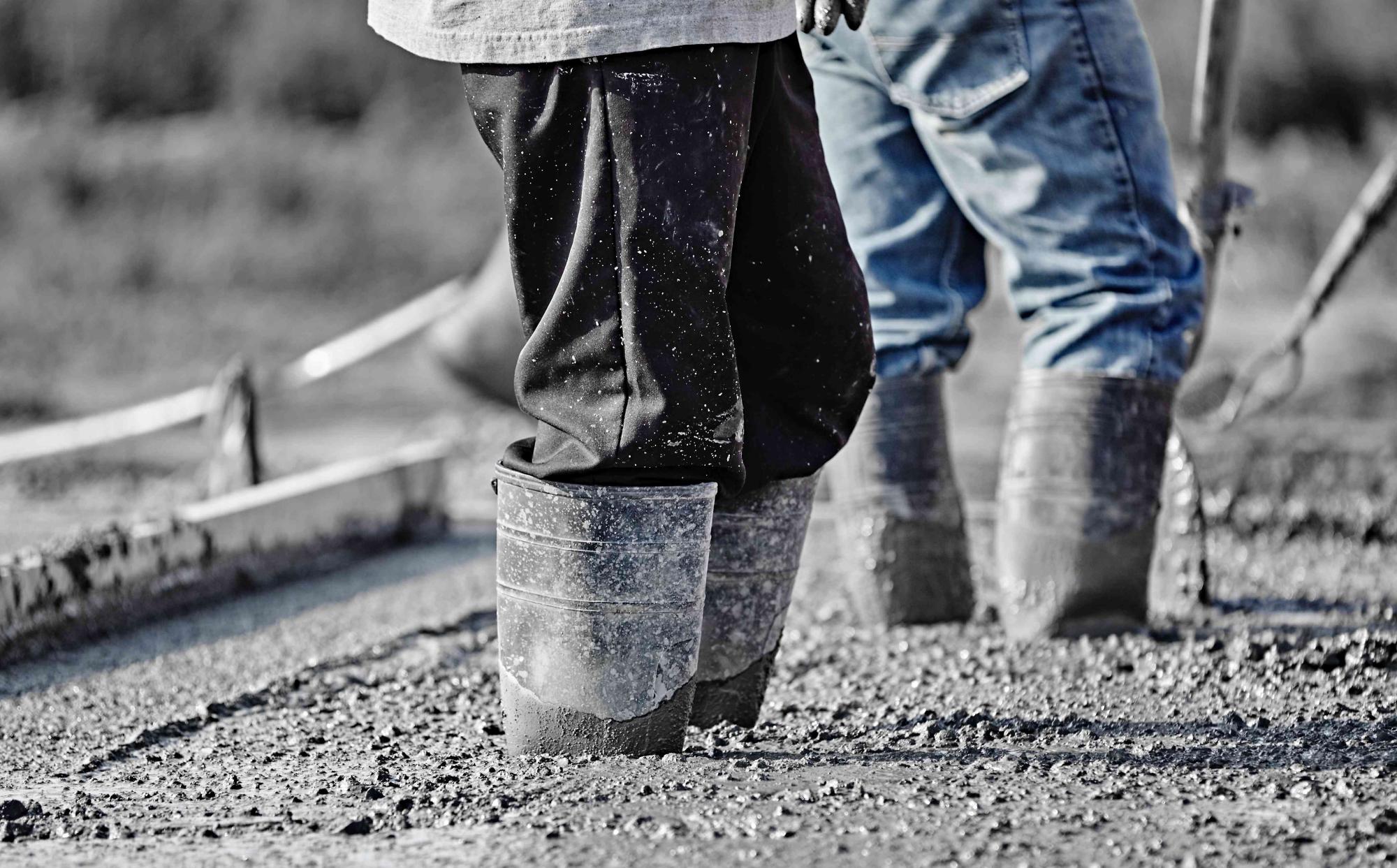 Concrete Workers In Heavy Boots Working In New Wet Concrete.